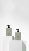 Two sage-green Curlyss pump bottles on white geometric plinths