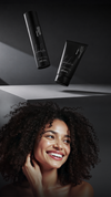 Smiling Black woman with curly hair beside black haircare products
